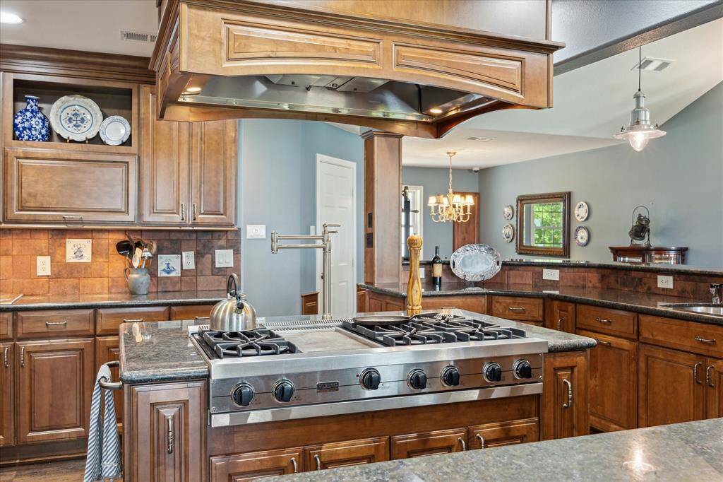 The "control" side of the Viking commercial grade 6-burner gas cook top with griddle. Built-in cookie sheet and spice cabinets are at each side of the island with pot & pan storage below the cook-top. The island also features a pot-filler faucet. Horizontal, open face and 42" upper cabinets are shown at the opposite side of the kitchen.