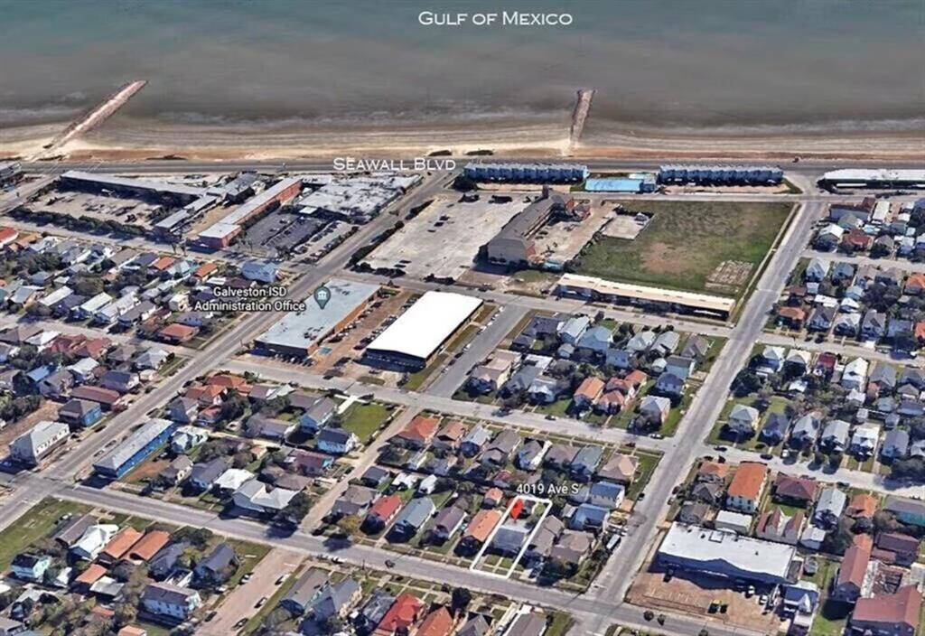 This aerial photo showcases a coastal neighborhood in Galveston, Texas, with proximity to the Gulf of Mexico. The area features residential homes, commercial buildings, and the Galveston ISD Administration Office, all near Seawall Boulevard. The beach and ocean proximity make it an appealing location.