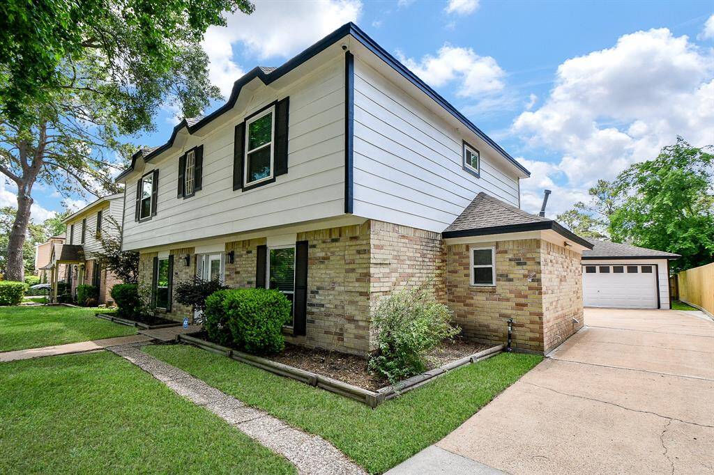 The front yard is beautifully landscaped with lush green grass, carefully placed bushes, and mature trees—one of which stands prominently in the foreground, providing shade and enhancing the property's curb appeal.