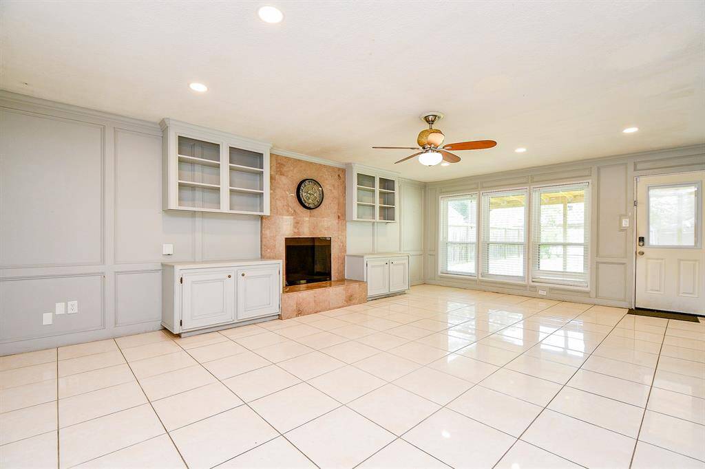 A modern, spacious living area filled with natural light,  Large windows on the left side allow sunlight to flood the room, complementing the sleek, glossy white tile flooring
