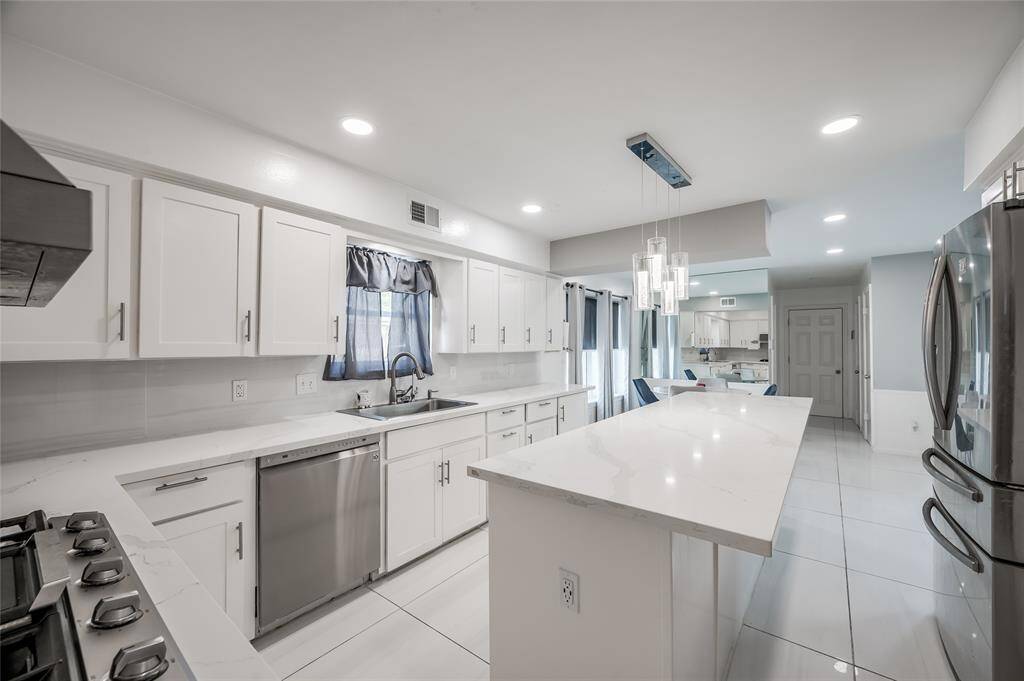 The island provides an ideal surface for meal prep, serving, and entertaining. The pristine white tiles on the floor and backsplash enhance the kitchen's bright and airy feel, making the space look fresh and inviting. This minimalist design not only exudes contemporary elegance but also offers a versatile backdrop for your personal style and culinary needs.