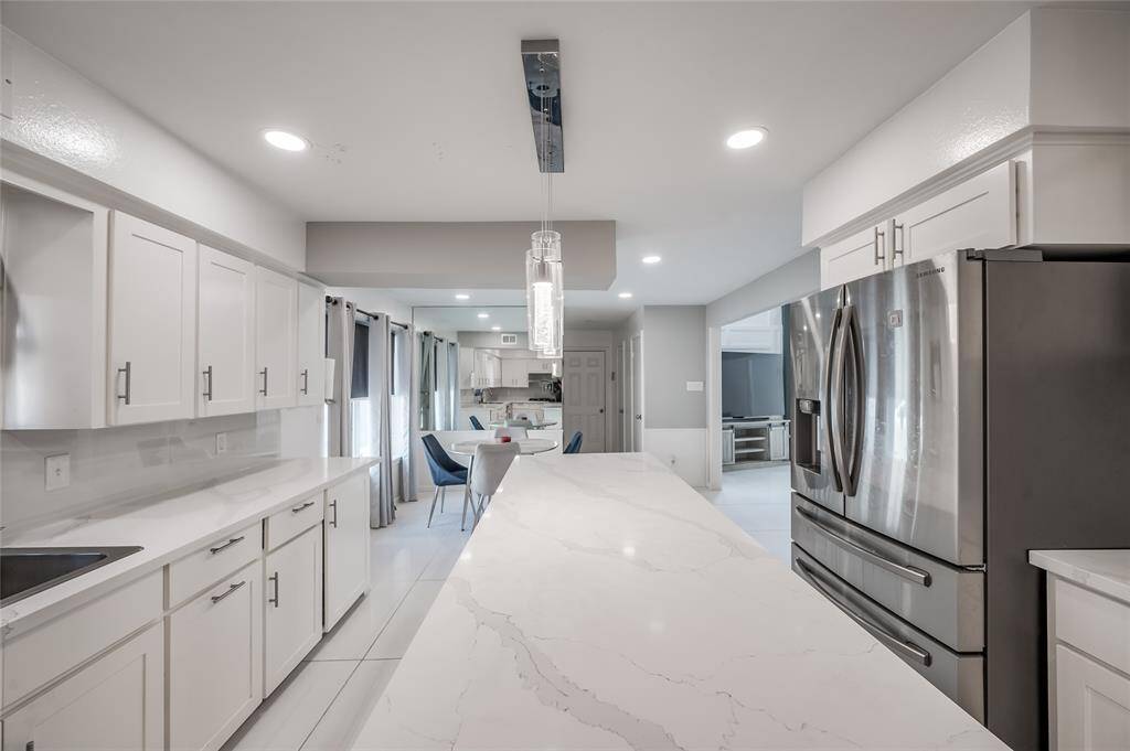 Step into this elegantly designed kitchen, where the clean, sleek lines and white tile flooring create a sophisticated, modern aesthetic. The centerpiece is a spacious island that offers ample counter space for meal preparation and casual dining.