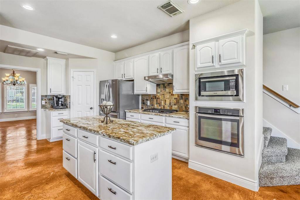 The large central island offers ample drawers and cabinet space. Additional features include recessed lighting, a built-in microwave above the single oven, and a spacious pantry for all your storage needs.