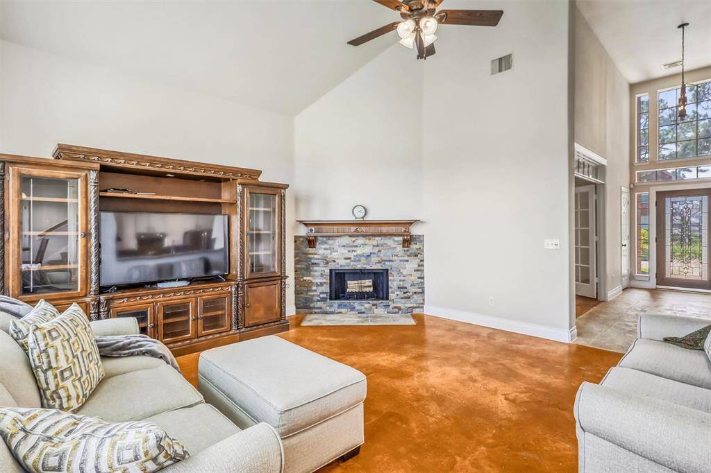 The vaulted ceiling adds dimension and architectural interest, creating a grand sense of space, while the striking stacked stone fireplace with a custom mantle becomes a captivating focal point in the room.
