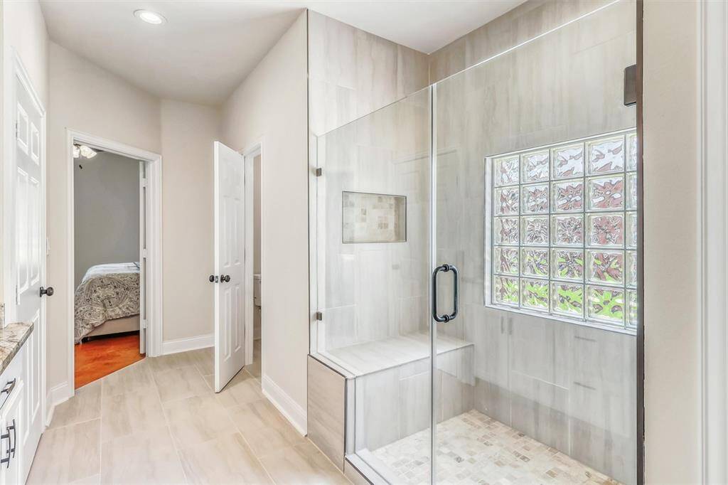 The remodeled walk-in shower is a standout feature, with a neutral tile surround that extends to the ceiling, accented by stunning tile floors and a cutout showcasing the same elegant accents. Enjoy the added comfort of a built-in bench seat, and experience the modern touch of frameless glass enclosure.