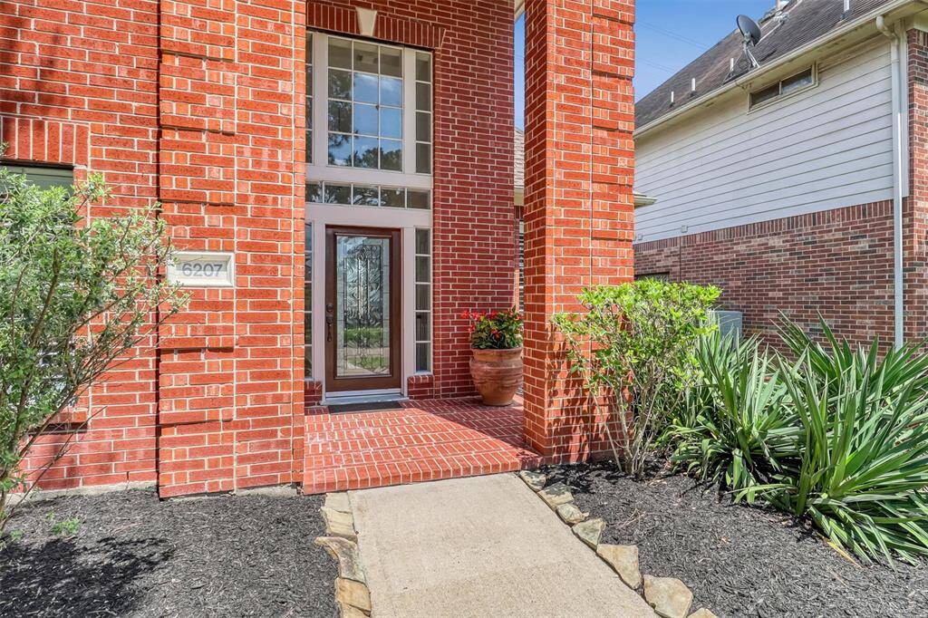 Follow the beautifully landscaped pathway to a grand two-story front porch with timeless brick flooring. A leaded glass front door, framed by transom and sidelight windows, creates a warm and elegant welcome.
