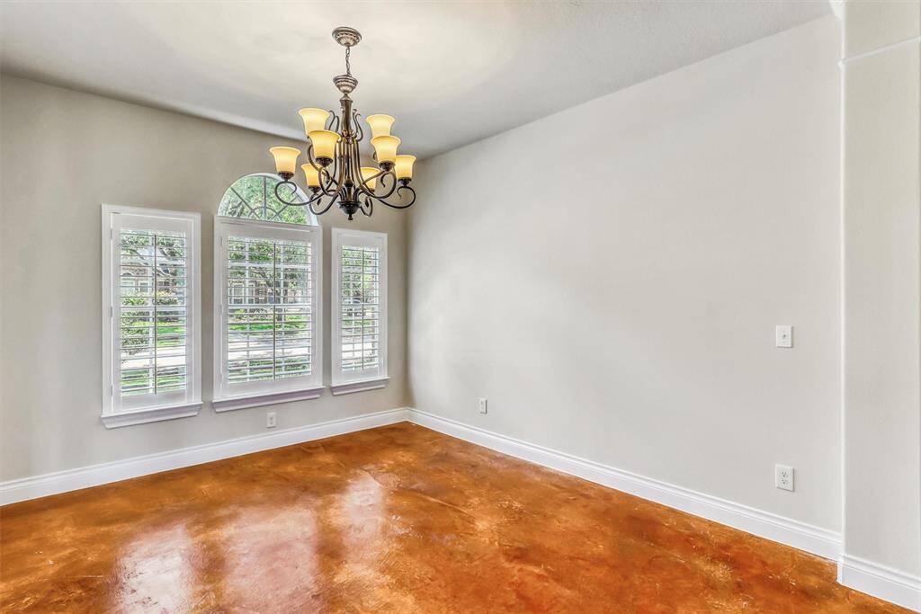To the left of the entry, the formal dining room impresses with a striking chandelier, fresh neutral paint, and three large windows—including a beautifully arched center window—all enhanced by classic plantation shutters.