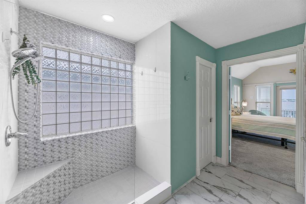 This bathroom features a modern walk-in shower with textured glass tiles and a built-in bench. The space is bright, with a large frosted glass window for natural light.
