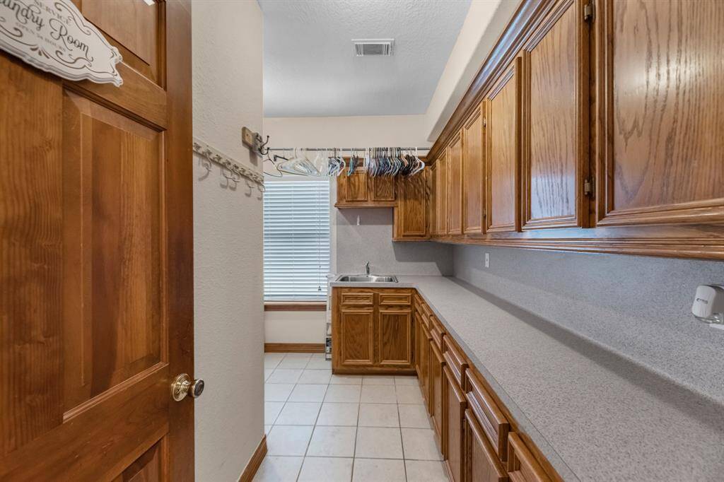 Spacious first-floor laundry room with ample cabinets, a convenient sink, and washer/dryer area to the left.