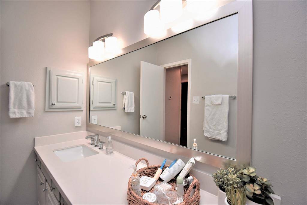 Wide mirror with wall mounted light, white countertops and cabinetry.