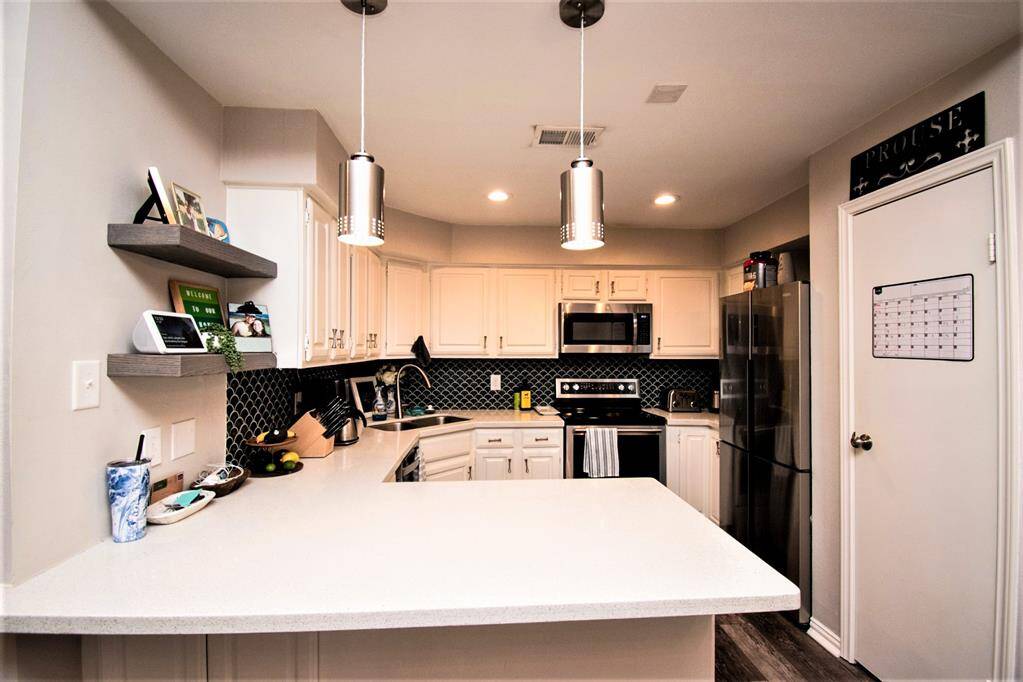 Kitchen with breakfast bar, gleaming white countertop, beautiful backsplash and white cabinetry.