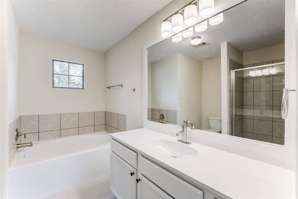 Freshly updated vanity and oversized mirror in the primary bathroom, with easy access to both the shower and bedroom.