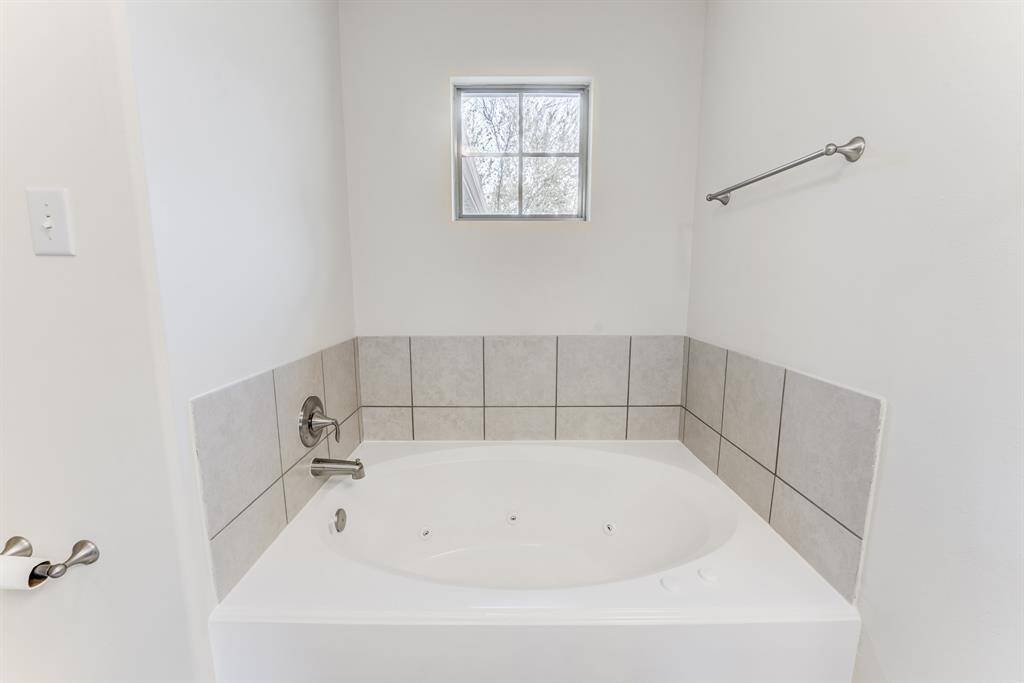 Enjoy a spa-like experience with a deep soaking garden tub, surrounded by neutral tile and a private window for natural light.