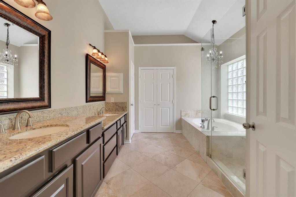 Retreat to your primary bath, complete with double sinks, a vanity, jetted tub with a chandelier overhead, oversized shower, beautiful granite, and custom mirrors.