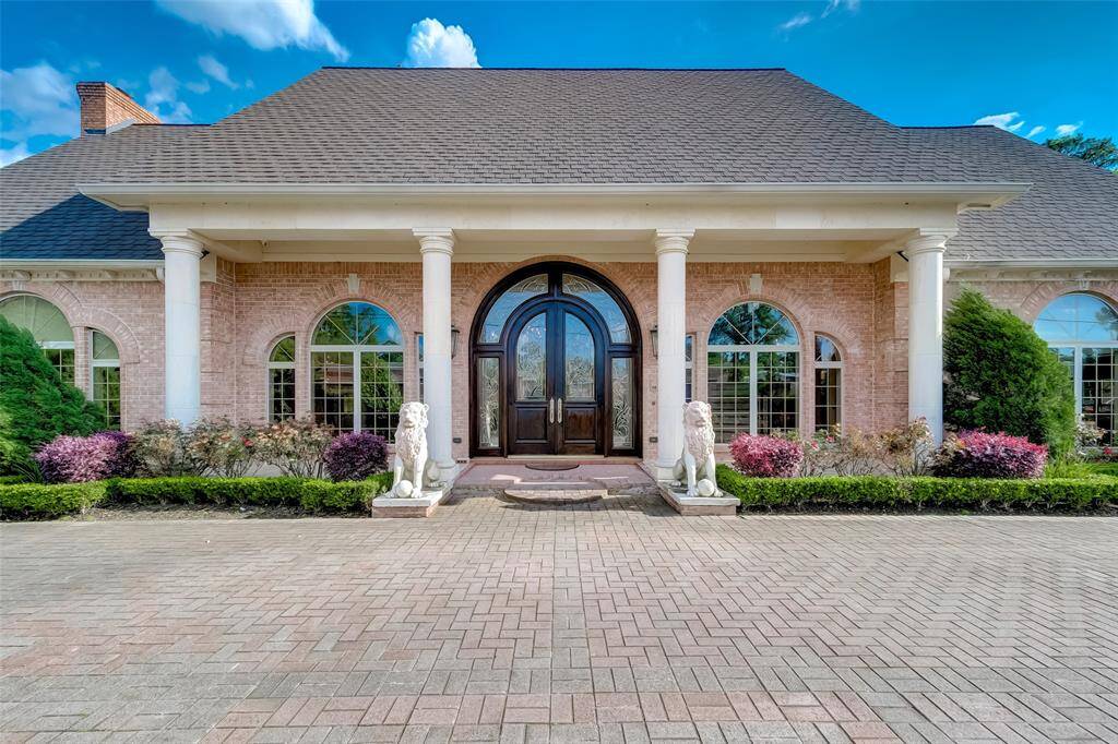 Stunning entrance with elegant columns and stately double doors, framed by lush landscaping for a luxurious welcome.
