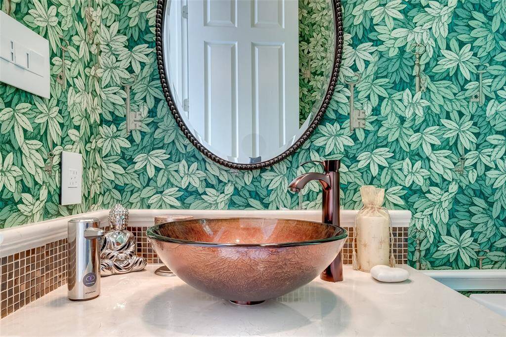 Discover sophistication in this stylish powder room, featuring designer wallpaper and a stunning glass vessel sink.