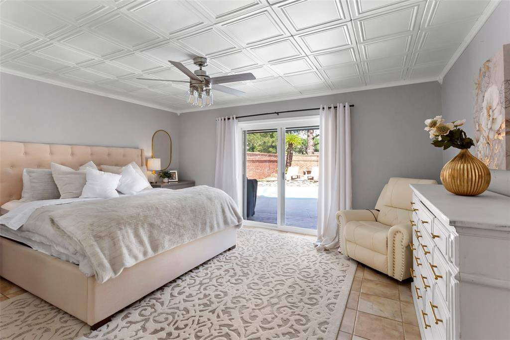 The primary suite features coffered ceiling providing a a high-end look. The sliding glass doors provide direct access to the pool area.