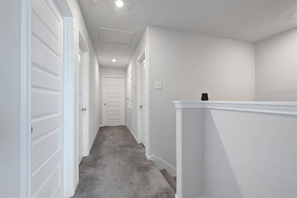 Bright upstairs hallway with carpeted flooring, access to bedrooms, and recessed lighting, offering a modern and welcoming feel.