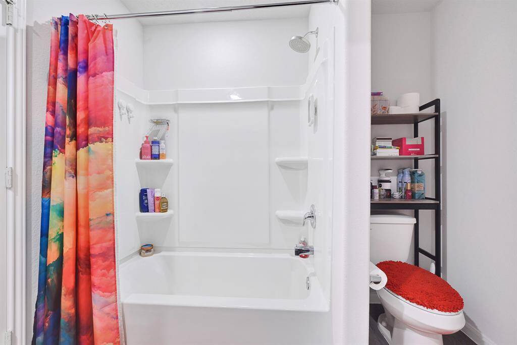 Primary bathroom features a tub/shower combo with built-in shelves, the space is bright and functional.