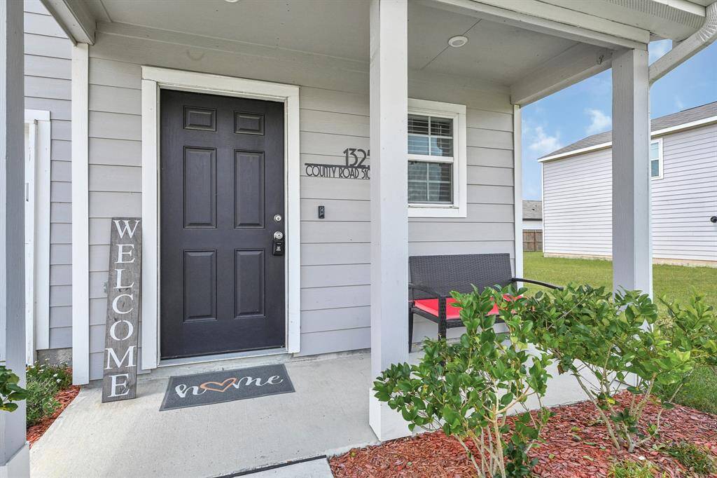 This welcoming front porch features a cozy seating area. The space is accented with greenery and mulch, creating a charming entrance to the home.