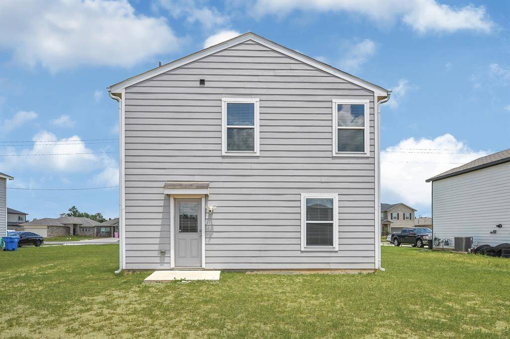 Modern two-story home with gray siding, large windows, and a small concrete stoop. The property is surrounded by a spacious lawn, offering a clear view of the neighborhood.