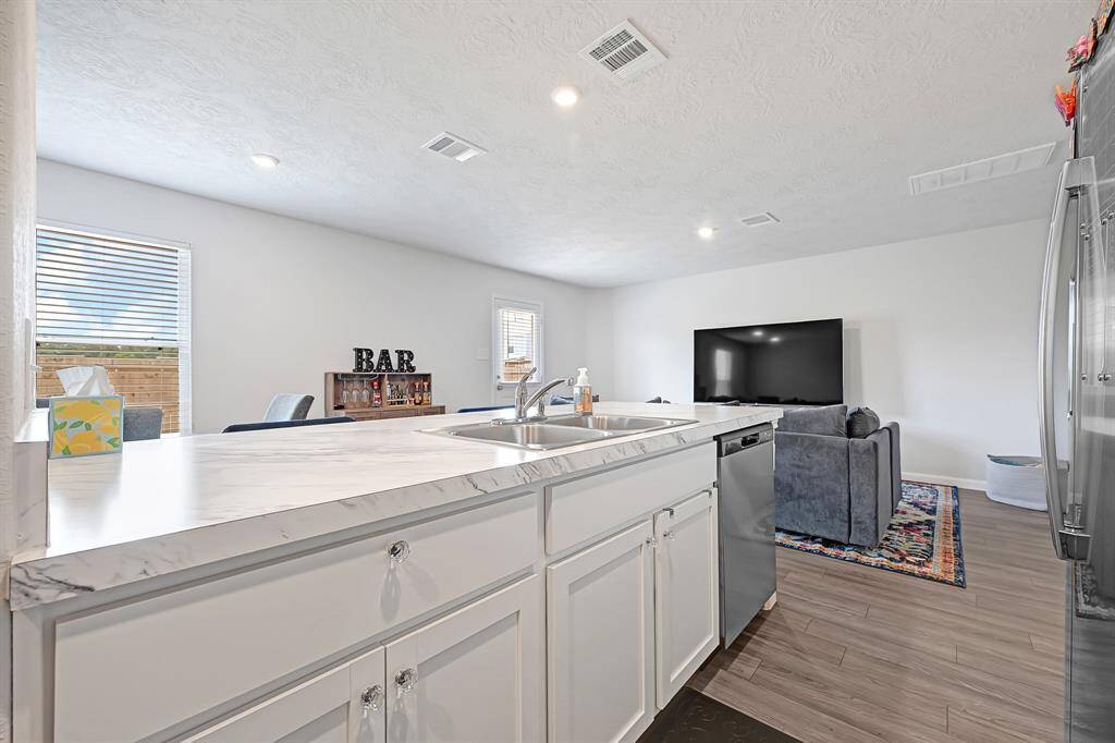Bright, open-concept kitchen and living area with modern appliances and a large countertop. Natural light floods the space through ample windows, highlighting the cozy seating area and space for a bar setup. Perfect for entertaining and everyday living.