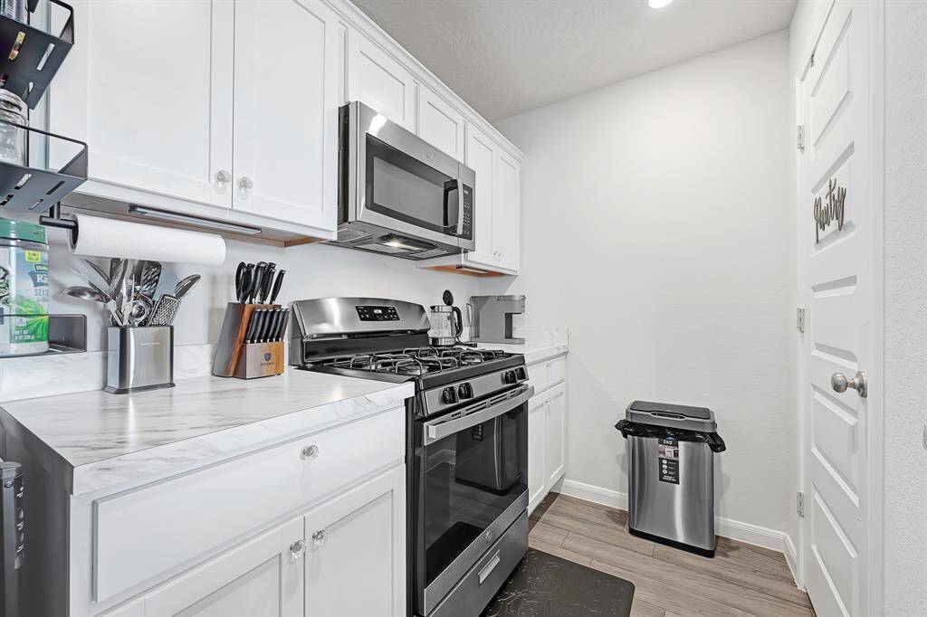 Modern & cozy kitchen with white cabinetry, stainless steel appliances, and a marble-look countertop. The space includes a gas stove, microwave, and ample storage. The kitchen has a sleek, clean design.