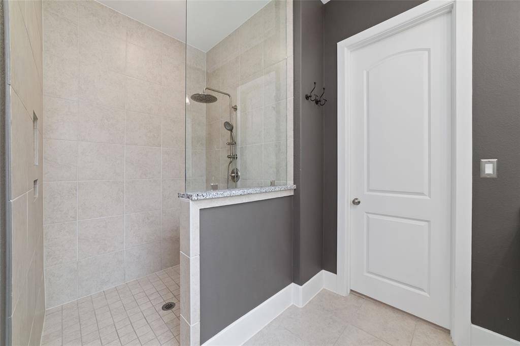 An extra large walk in shower with rain shower head, pony wall and glass panel providing a partial barrier to splash and enhancing the open feel of the space.