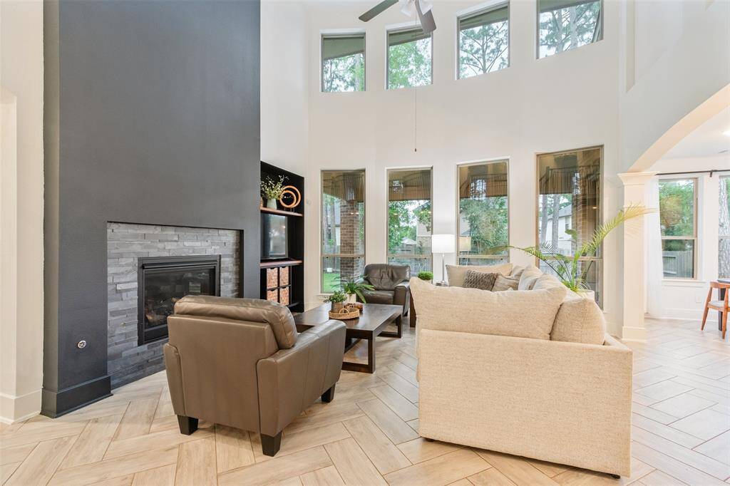 Bright and spacious living room with high ceilings and large windows offering plenty of natural light. Features a modern fireplace, cozy seating area, and stylish tile flooring. Perfect for comfortable living and entertaining.