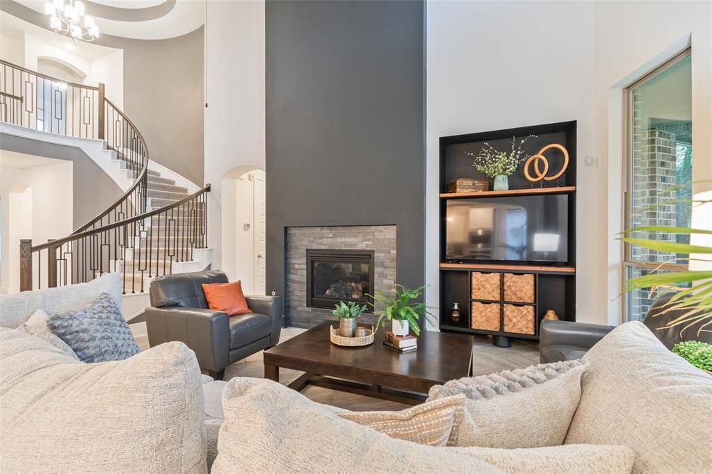This inviting living room features a modern fireplace, a stylish spiral staircase, and abundant natural light. A cozy seating area with neutral-toned furniture complements the contemporary decor, making it perfect for relaxation or entertaining.