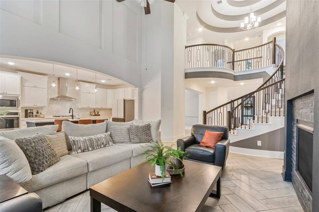 Spacious open-concept living area featuring a modern kitchen with white cabinetry and stainless steel appliances, a cozy sitting area with a sleek fireplace, and an elegant curved staircase leading to the second floor.