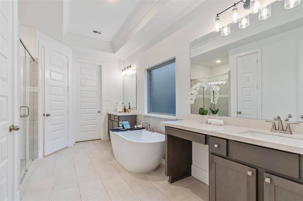 This spacious bathroom features a modern freestanding tub, dual sinks with sleek countertops and large mirrors.  The bright, neutral design is complemented by stylish lighting and ample cabinetry.