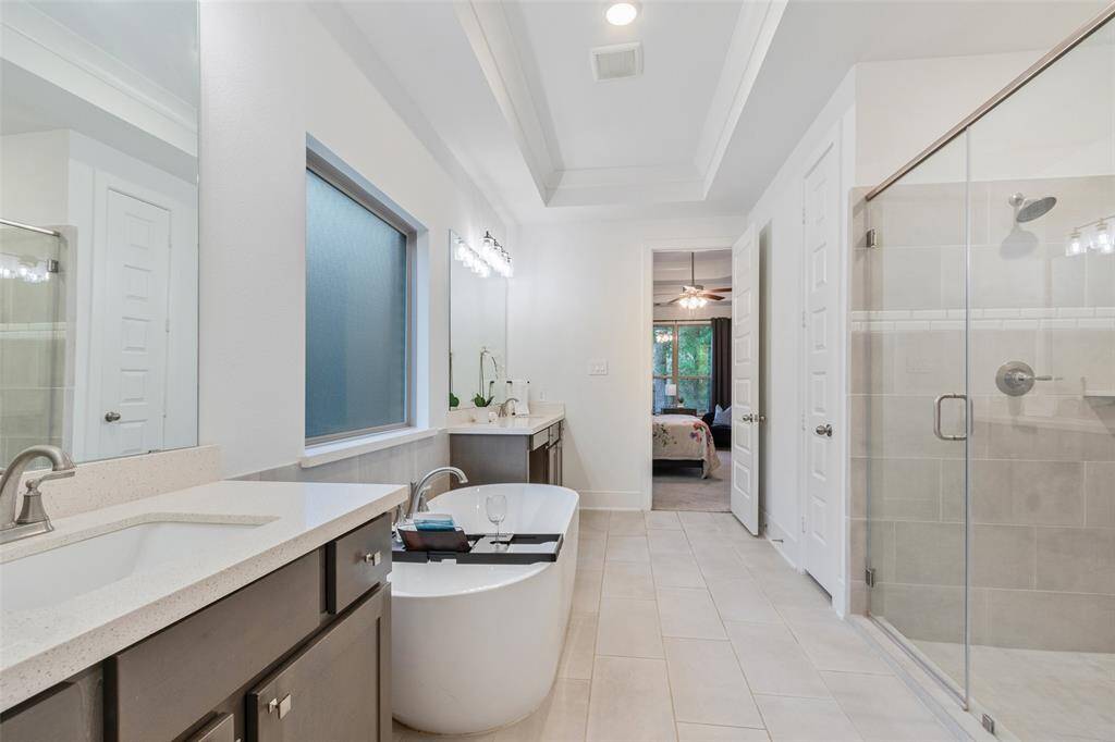 This photo showcases a modern, spacious bathroom featuring a freestanding tub, double sinks with quartz countertops, a large mirror, and a glass-enclosed shower. The neutral color palette and ample natural light create a serene atmosphere.