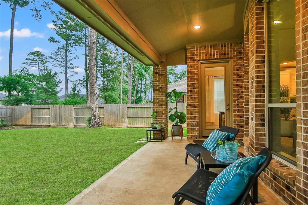 This photo showcases a spacious covered patio with brick walls and comfortable seating, overlooking a well-maintained, fenced backyard with tall trees offering privacy and a natural setting.