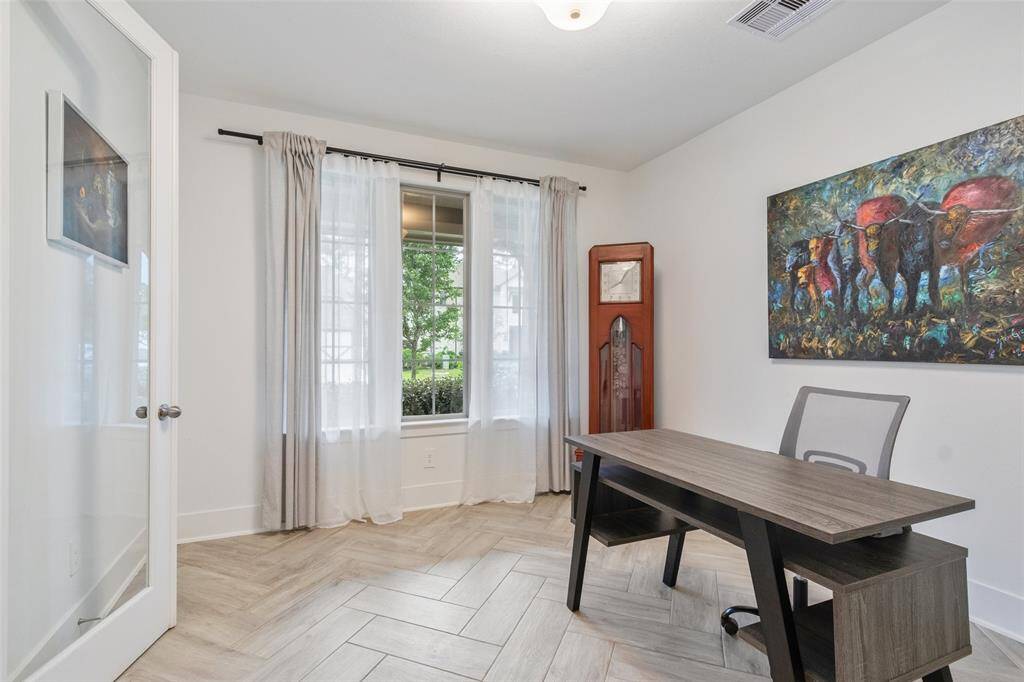 Bright home office with large window, glass door, and wood-look tile flooring.  This room would also make a great playroom, reading room or formal living space.