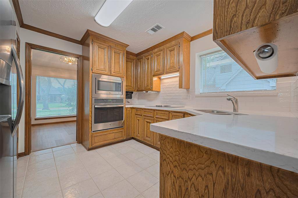 Louvered doors from the formal dining room lead into the kitchen, showcasing gorgeous solid hardwood custom cabinets with crown molding. The tile flooring, easy to maintain, adds a stylish, durable touch, completing the space with timeless appeal.