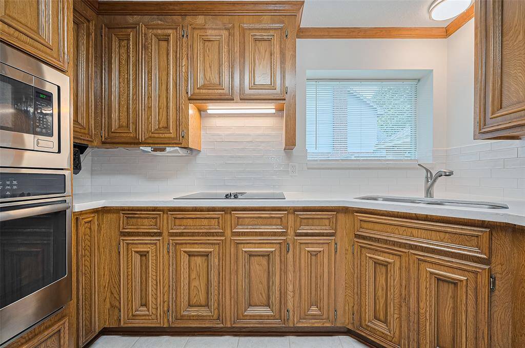 The kitchen is 10.10 x 8.10 and features gorgeous hardwood cabinets, updated in 2023 with sleek quartz countertops and a subway tile backsplash. A picture window overlooks the side yard and driveway, filling the space with natural light. The wide window ledge is perfect for growing violets or herbs, adding a touch of greenery to the kitchen.