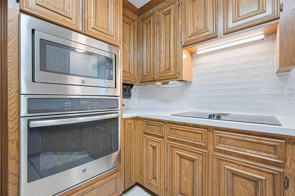 It is equipped with a GE stainless steel microwave and oven combination, featuring convection capabilities for faster, more even cooking. Convection cooking circulates hot air, reducing cook time and enhancing flavor. To the right, a GE downdraft glass-top cooktop vents to the exterior, with an overhead light to illuminate the area during cooking.