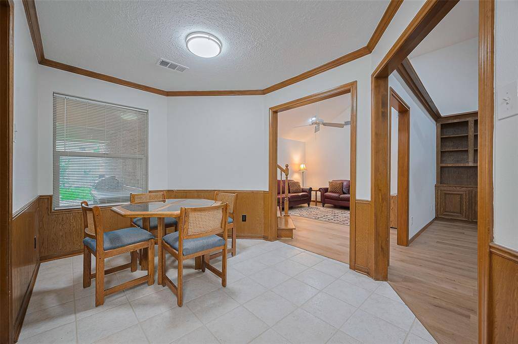 The breakfast area, measuring 12'2" x 8'7", features a tile floor for easy cleanup and crown molding for a polished touch. Doorways open into the living and family rooms, creating a seamless flow. Along the paneled far wall, a hidden storage space beneath the staircase offers a clever spot for bulky items like paper towels, toilet paper, or seasonal supplies.