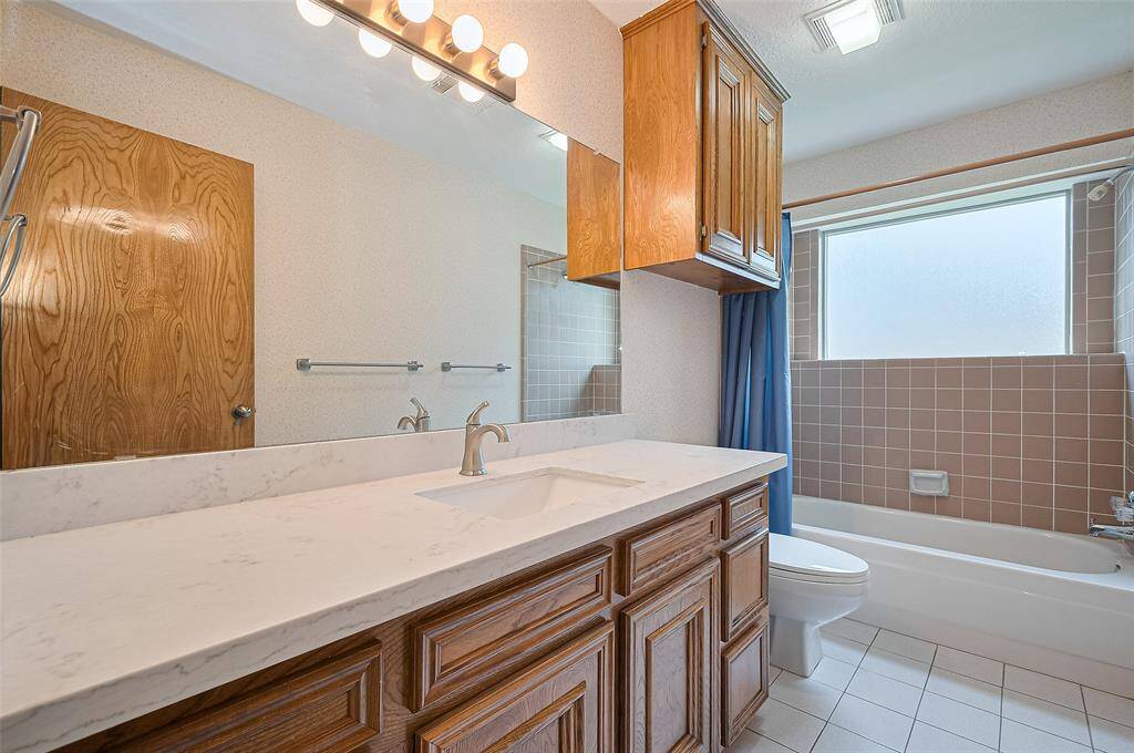 Bath #2, measuring 10'9" x 4'11", features a single sink with a quartz countertop (2023) and a hardwood vanity cabinet with 6 operable drawers—ideal for children sharing a bath. A wall mirror was also updated in 2023. The tub-shower combo includes tiled shower walls, and there's an over-commode storage cabinet for added convenience. The tile floor complements the space, and a linen closet in the hallway provides additional storage.