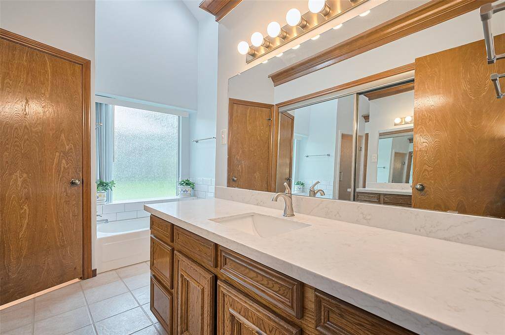 The left-side vanity area features hardwood cabinetry with 6 operable drawers for ample storage. It includes a single sink with a quartz countertop (2023) and a wall mirror (2023). Opposite the sink, a sliding mirror closet offers additional storage space. This private vanity and dressing area creates a personal, organized space just for you. The bath also includes a private water closet with the commode for added comfort and privacy.