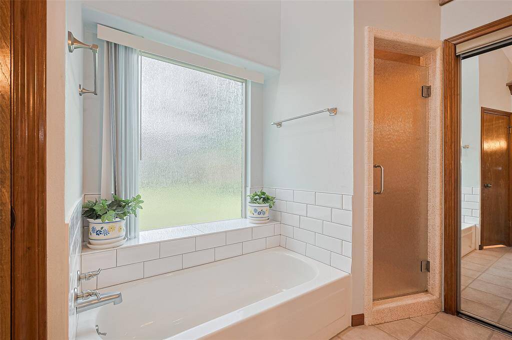 The Owner's Ensuite Bathroom features a tub with two double pane rainglass privacy windows—one in the water closet and the other over the tub, allowing plenty of natural light while maintaining privacy. The tub’s tile surround was replaced in 2024, adding a fresh touch. A large, lighted walk-in shower with a rainglass shower door (2023) completes the space. It's a beautiful, relaxing bath designed for comfort and tranquility.