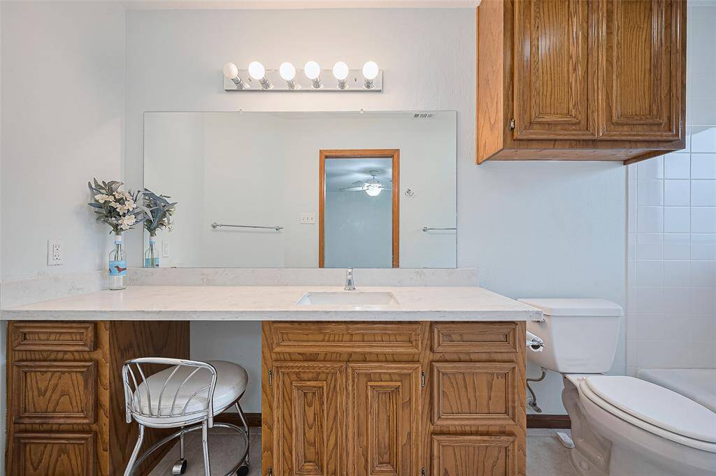 Bedroom #4's ensuite bathroom features a wooden vanity with 6 operable drawers, providing ample storage and a convenient makeup knee space. The single sink is set in a quartz countertop (2023), complemented by a wall mirror (2023). Additional storage is available in a cabinet above the commode, and the tile floor adds a durable, easy-to-maintain touch.