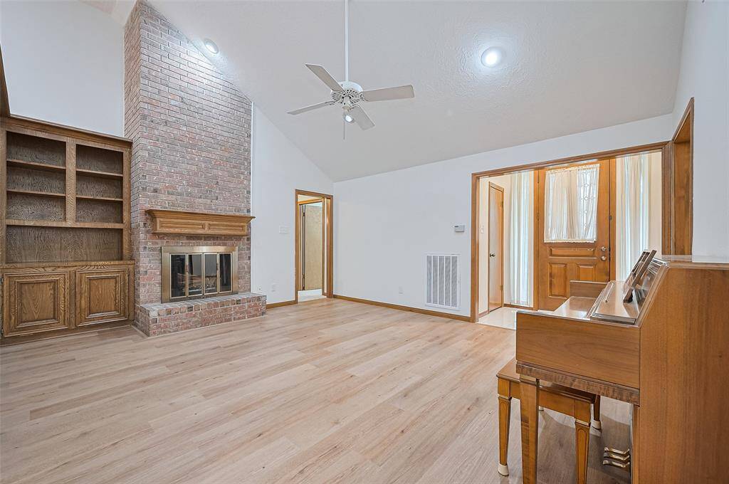 The foyer opens into a spacious living room with a vaulted ceiling, recessed LED lighting, and a ceiling fan for year-round comfort. Durable LVP flooring, updated in 2023, flows through the dining, living, and family rooms—offering the look of hardwood with water resistance and easy maintenance. A doorway beside the fireplace leads to the primary suite and two secondary bedrooms.