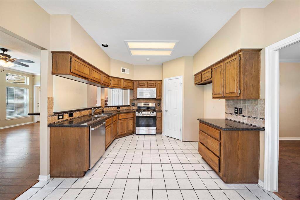 This kitchen features wood cabinets, stainless steel appliances, and granite countertops. It has a tiled floor and an open layout.