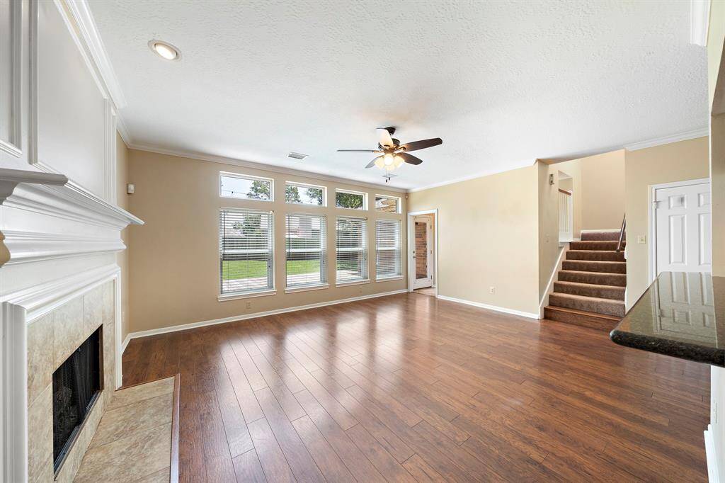 Bright and spacious living room featuring hardwood floors, a cozy fireplace, and large windows for natural light. It opens to a staircase and has access to a backyard view.