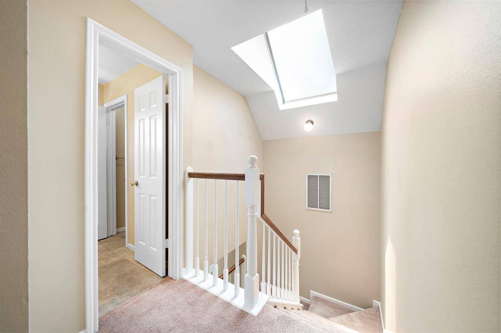 This photo shows a bright, carpeted staircase landing with a skylight providing natural light.