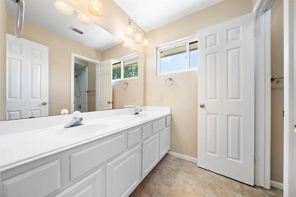This is a bright and spacious bathroom featuring a double vanity with ample storage, large mirrors, and modern lighting. A window provides natural light.