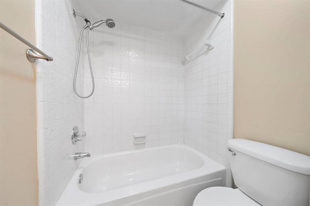 This bathroom features a clean, white tiled shower and bathtub combo, complete with a handheld showerhead.