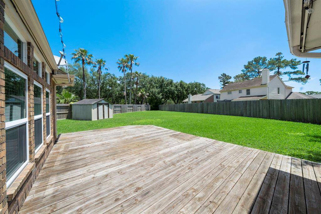 This photo shows a spacious backyard with a large wooden deck, well-maintained lawn, and a storage shed, surrounded by a fence for privacy.